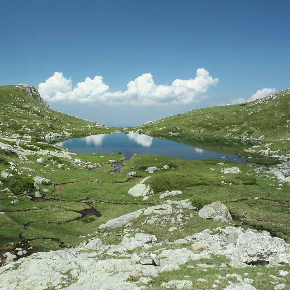 Blue skies and green hills surround a lake in Rila, Bulgaria